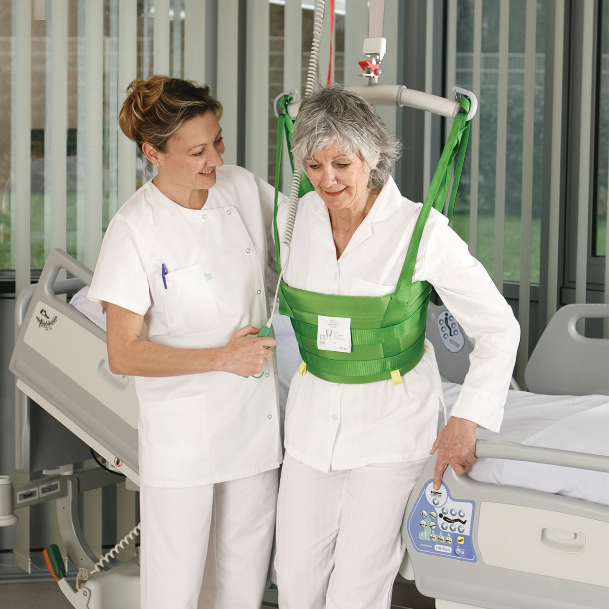 Un clinicien aide un patient à marcher dans une chambre d'hôpital avec lève-personne plafonnier de Hillrom et un dispositif MasterVest
